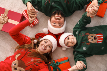 Happy parents with their little son in Santa hats holding hands at home on Christmas eve, top view