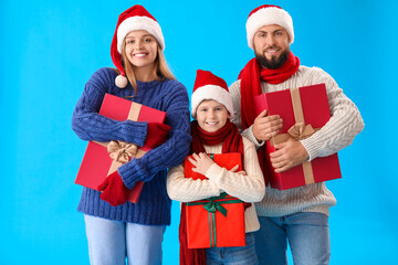 Fototapeta premium Happy parents with their little son in Santa hats and Christmas gifts on blue background