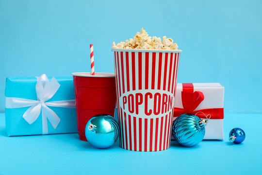 Bucket of popcorn, cup, presents and Christmas balls on blue background