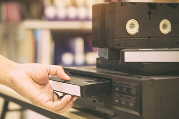 Close-up hand chooses and put or insert video cassette tape VHS on video tape player concept of vintage electric retro style and electronic appliances multimedia player device old fashioned.