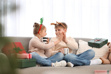 Little children with cups of cocoa giving each other high-five at home on Christmas eve