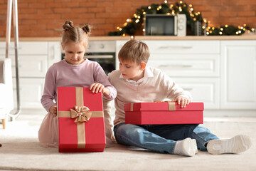 Little children with Christmas presents sitting on floor in kitchen
