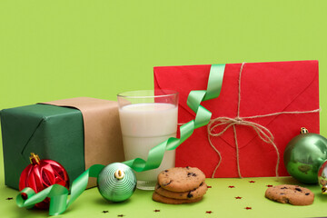 Letter to Santa with glass of milk, cookies, present and Christmas decor on green background