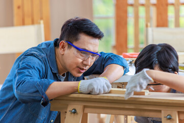 Asian professional carpenter engineer dad teaching young boy son in jeans outfit with gloves safety...