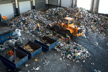 Bulldozer collects rubbish in warehouse of recycling plant