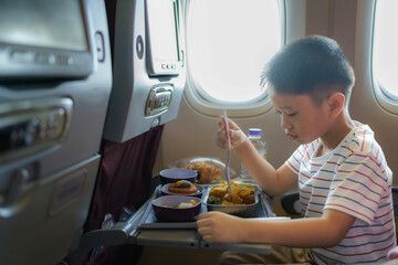 Asian Child in airplane window seat. Kids flight meal. Children fly. Special inflight menu, food...