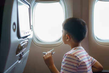 Asian children look at the aerial view of the sky and clouds outside the plane window while sitting...