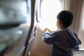 Asian children look at the aerial view of the sky and clouds outside the plane window while sitting...