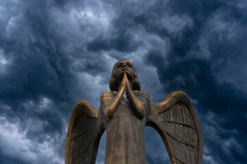 Detail of beautiful bronze statue of an angel with wings against the dark sky with clouds....