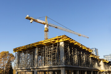 Yellow tower crane on the monolithic residential buildings' construction site.	