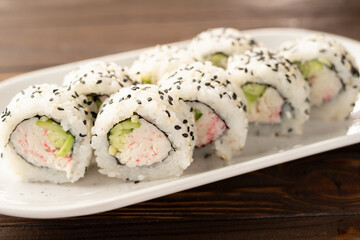 Maki California sushi with surimi crab, cucumber and sesame seeds on white plate in sushi bar. Japanese food