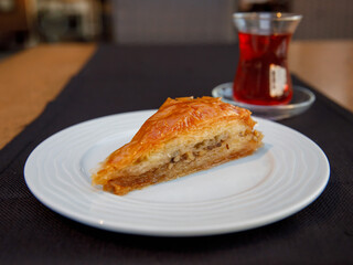 Piece of Carrot Slice Baklava (Turkish: Havuc Dilim Baklava) on white plate with glass of tea on...