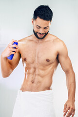 Fototapeta premium Spray, clean and body of a man with deodorant after a shower against a grey studio background. Wellness, happy and young model with a smile for a fragrance product, health and happiness for hygiene