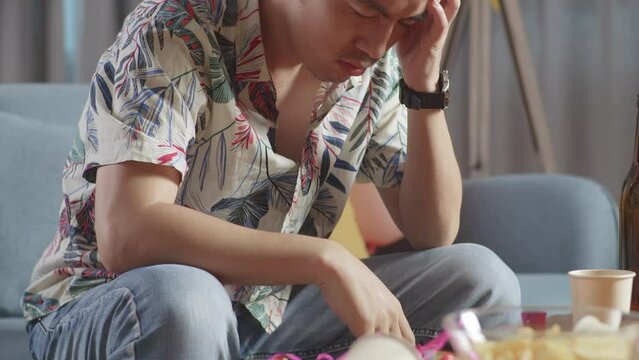 Close Up Of A Drunk Asian Man Sitting On A Sofa After Having A Party At Home
