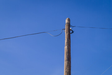 A wooden pole of a power line against a blue sky. Part of the external power transmission network....