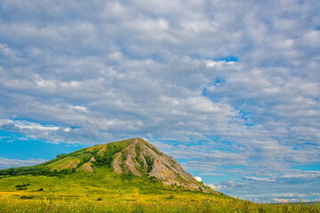 Green valley with pasture, relic mountain Shihan, blue cloudy sky in  sun. Summer landscape.