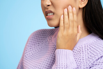 Cropped view of unhappy teen girl in hoodie touching sore cheek, frowning from acute pain