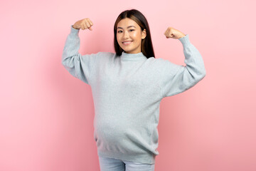 Portrait of pregnant asian woman raising arms showing biceps as metaphor of female power