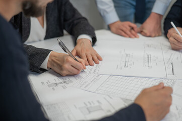 Close-up of the hands of four colleagues with blueprints on the table in the office. Brainstorming of engineers and architects.