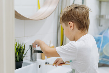 cute 5 years old boy brushing teeth with bamboo tooth brush in bathroom rinsing brush with water