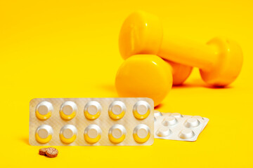 silver plates with tablets and tablets without packaging on the background of yellow dumbbells.