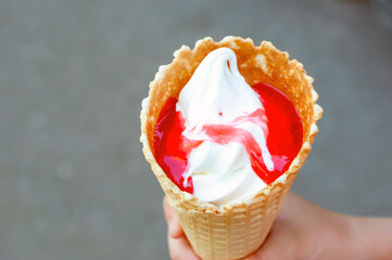 man's hand holds a waffle cup of cream ice cream with a red additive on the street, copy space.