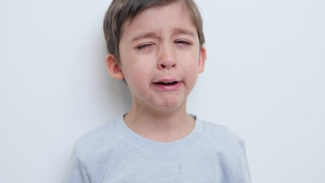 portrait of an offended child a five year old boy crying loudly against a white wall in a room