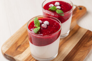 Two portion coconut Panna cotta with cranberry sauce in glasses on a white wooden table. Healthy vegan dessert.