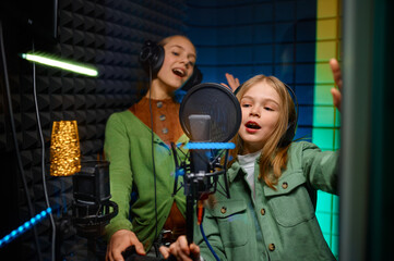 Happy girls wearing headphones singing in record studio