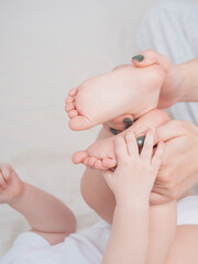 Baby's small legs in mom's hands, close-up. The concept of family happiness, loving parents. Baby care, massage. Background for Mother's day, baby's day. Touching mother and child