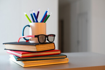 Stack of books with colored spines, colorful pencils in a cup
