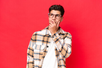 Young caucasian handsome man isolated on red background having doubts and with confuse face expression