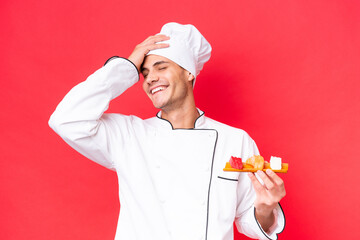 Young caucasian chef man holding sashimi isolated on red background smiling a lot