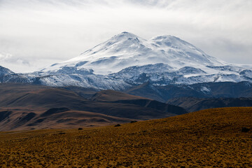 Big mountain Elbrus on the background of a cloudy sky. View from a large plateau and steep cliffs.