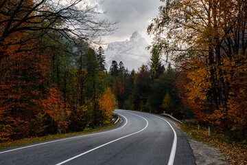 Winding road in the autumn forest against the backdrop of mountains