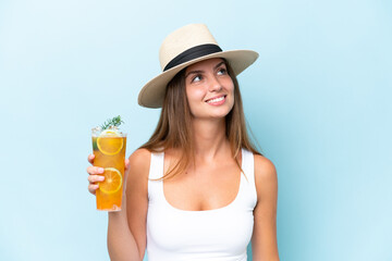 Young beautiful woman holding a cocktail isolated on blue background looking up while smiling