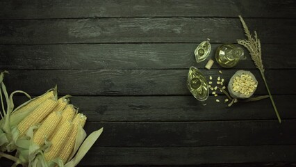 On a black wooden table is an armful of corn on the cob, as well as corn oil in various dishes, corn kernels and the top of the stem .Camera movement over the table from right to left. Flat lay.