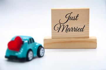 Mini toy car carrying red heart shape with Just Married text on wooden blocks background. Newly wed concept.