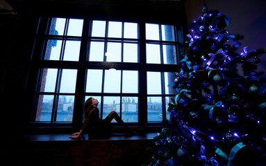 Silhouette of a girl sitting at a large panoramic window in the late evening