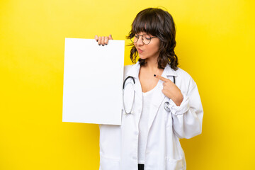 Young doctor latin woman isolated on yellow background holding an empty placard and looking it