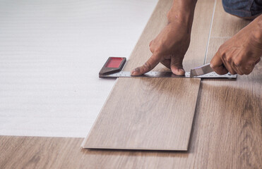 A technician is cutting luxury vinyl floor tiles with a cutter to lay the floor before placing it...