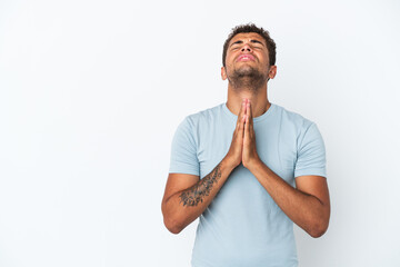 Young handsome Brazilian man isolated on white background keeps palm together. Person asks for something