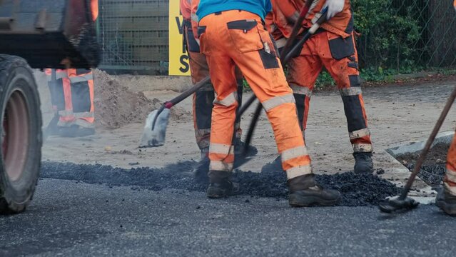 Roadwork Physical Workers in Protective Work Wear Repairing Street Tarmac Surface with Hot Asphalt