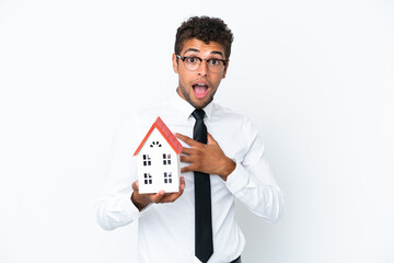 Young business Brazilian man holding a house toy isolated on white background surprised and shocked...