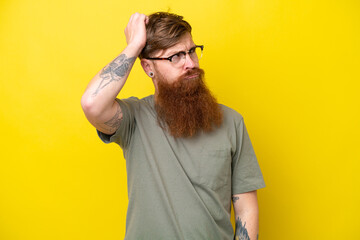 Redhead man with beard isolated on yellow background having doubts while scratching head