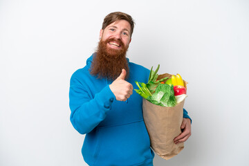 Redhead man with beard holding a grocery shopping bag isolated on white background giving a thumbs up gesture