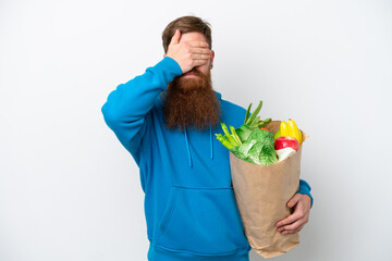 Redhead man with beard holding a grocery shopping bag isolated on white background covering eyes by hands. Do not want to see something