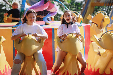 Teenage girls ride on carousels in the park.