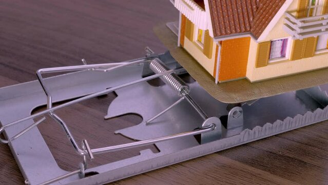 A model house used as bait on a spring loaded trap. Concept of the lure of property, with a danger warning as to burdens like rent, mortgage, bills, upkeep, etc.