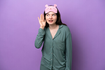 Young Russian woman in pajamas isolated on purple background listening to something by putting hand on the ear
